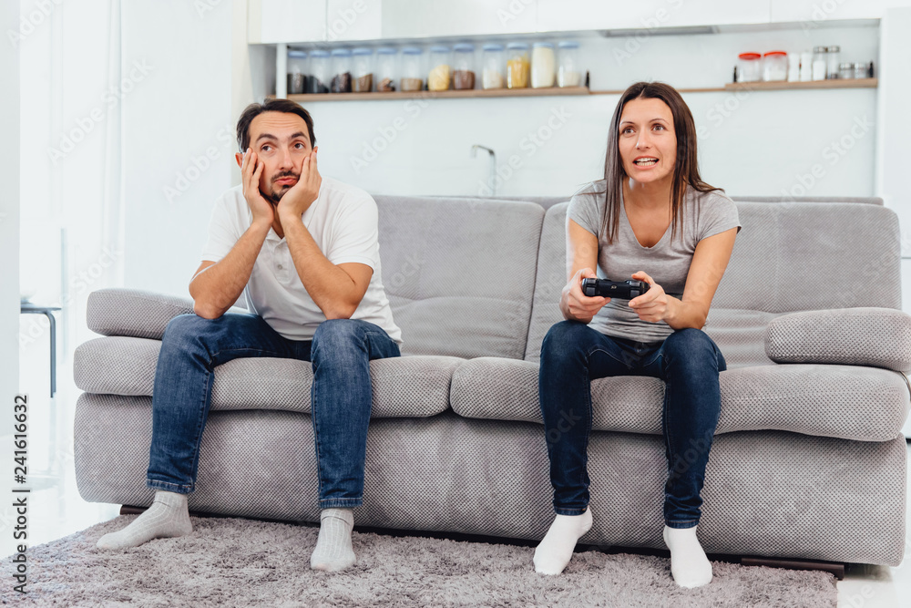 The wife plays the game while the man just sits The wife plays the game while the man just sits