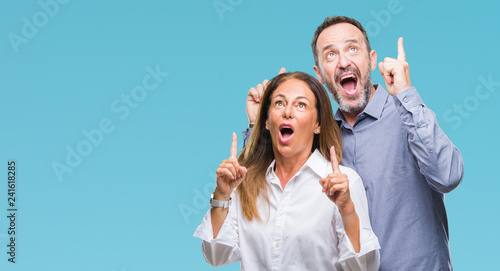 Middle age hispanic business couple over isolated background amazed and surprised looking up and pointing with fingers and raised arms.
