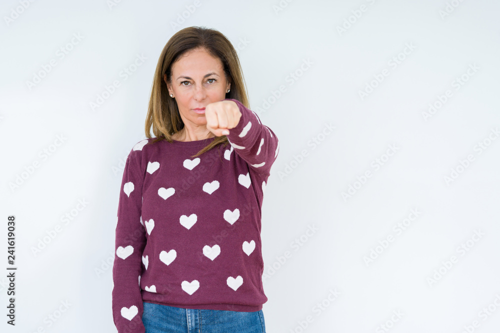 Beautiful middle age woman wearing heart sweater over isolated background Punching fist to fight, aggressive and angry attack, threat and violence Beautiful middle age woman wearing heart sweater over isolated background Punching fist to fight, aggressive and angry attack, threat and violence