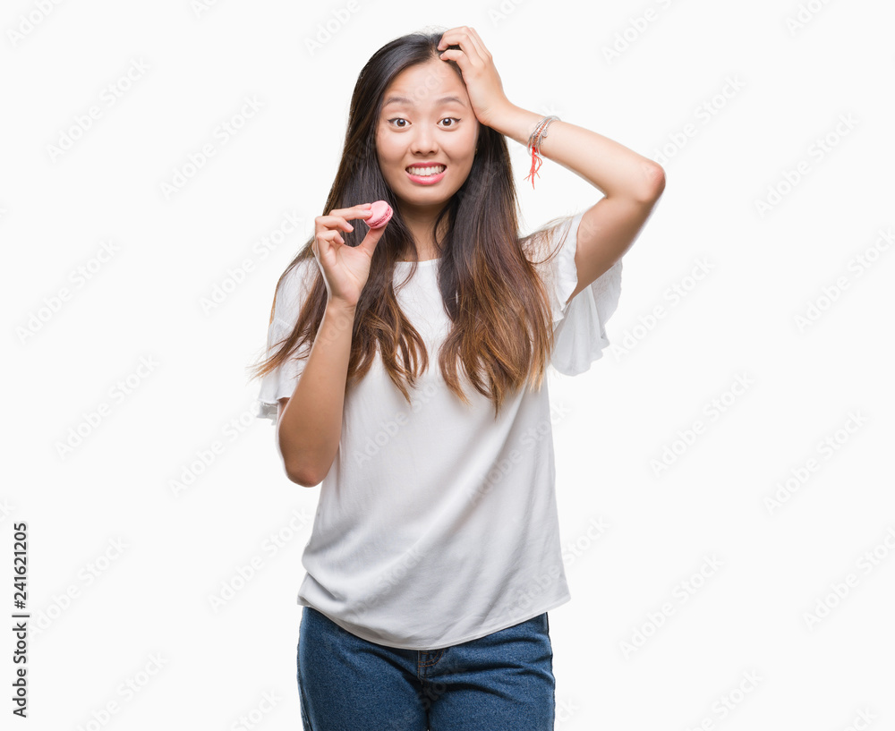 Young asian woman eating pink macaron sweet over isolated background stressed with hand on head, shocked with shame and surprise face, angry and frustrated. Fear and upset for mistake. Young asian woman eating pink macaron sweet over isolated background stressed with hand on head, shocked with shame and surprise face, angry and frustrated. Fear and upset for mistake.