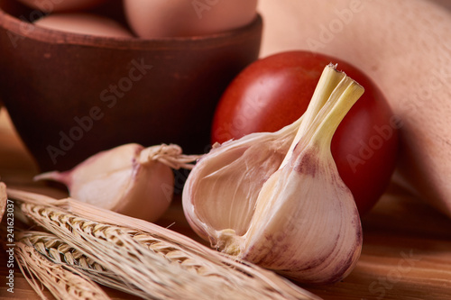 Bilde på lerret garlic on a wooden table with eggs in clay bowl, tomato, battledore and wheat sp