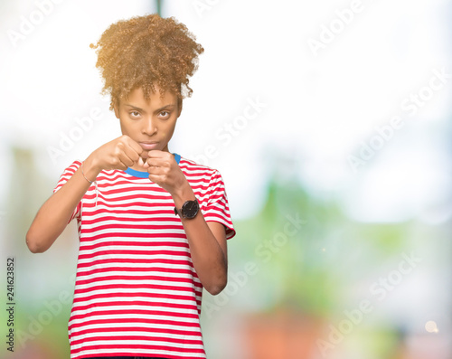 Beautiful young african american woman over isolated background Punching fist to fight, aggressive and angry attack, threat and violence © Krakenimages.com