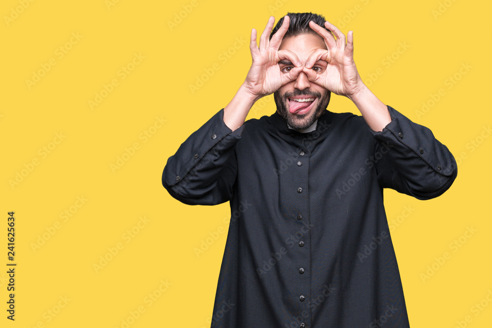 Young Christian priest over isolated background doing ok gesture like binoculars sticking tongue out, eyes looking through fingers. Crazy expression. Young Christian priest over isolated background doing ok gesture like binoculars sticking tongue out, eyes looking through fingers. Crazy expression.