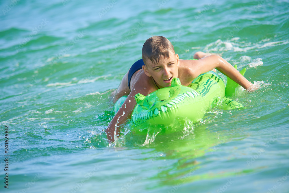 TEEN BOY SWIMMING IN THE SEA ON INFLATABLE TOY CROCODY