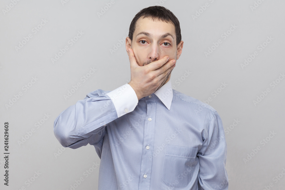 i will be quiet. Shocked handsome bristle businessman in classic blue shirt standing looking at camera with big eyes and covering his mouth. indoor studio shot, isolated on grey background copyspace. i will be quiet. Shocked handsome bristle businessman in classic blue shirt standing looking at camera with big eyes and covering his mouth. indoor studio shot, isolated on grey background copyspace.