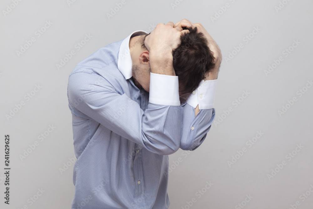 difficulties, failure or mistake. Portrait of handsome bristle businessman in classic light blue shirt standing and holding his head. indoor studio shot, isolated on grey background copyspace. difficulties, failure or mistake. Portrait of handsome bristle businessman in classic light blue shirt standing and holding his head. indoor studio shot, isolated on grey background copyspace.