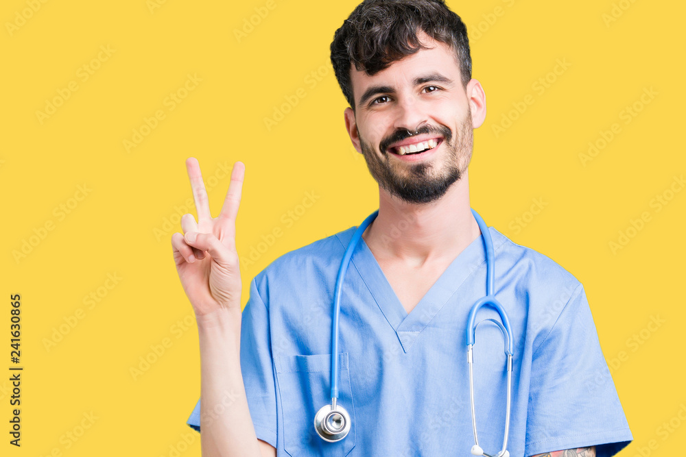 Young handsome nurse man wearing surgeon uniform over isolated background smiling with happy face winking at the camera doing victory sign. Number two. Young handsome nurse man wearing surgeon uniform over isolated background smiling with happy face winking at the camera doing victory sign. Number two.
