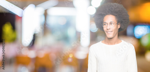 Young african american man with afro hair wearing glasses looking away to side with smile on face, natural expression. Laughing confident.