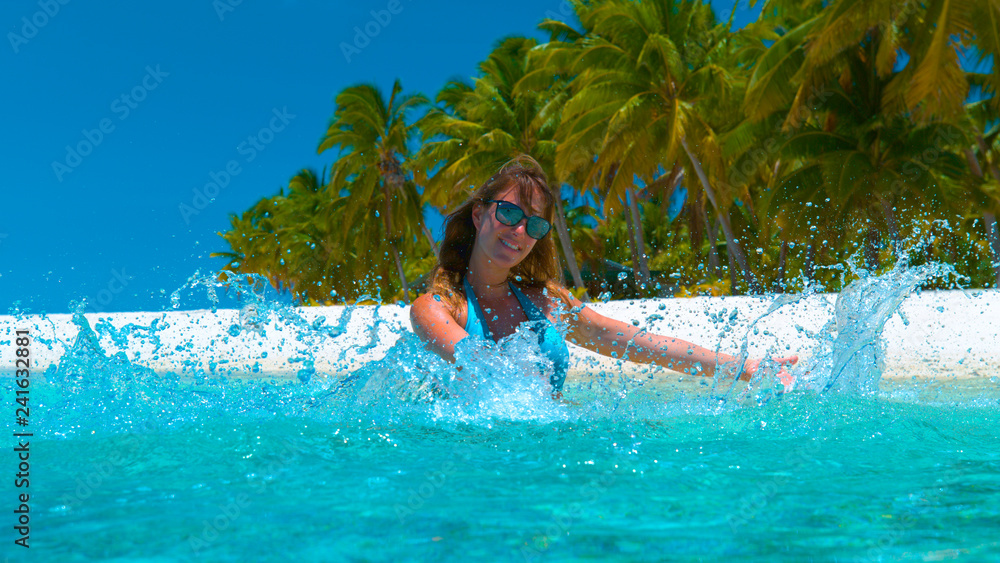 CLOSE UP: Tourist girl spraying sea water with her hands by beautiful shore.