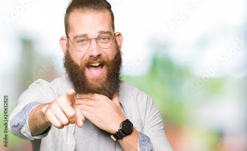 Young blond man wearing glasses Laughing of you, pointing to the camera with finger hand over mouth, shame expression