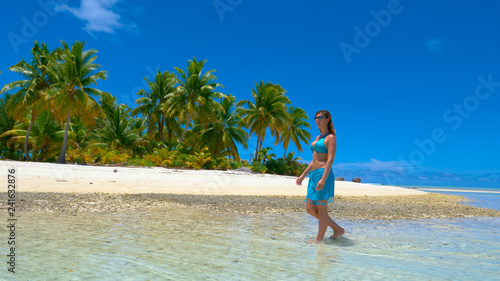 Young woman in bikini walking in the shallow ocean water and along sandy beach.