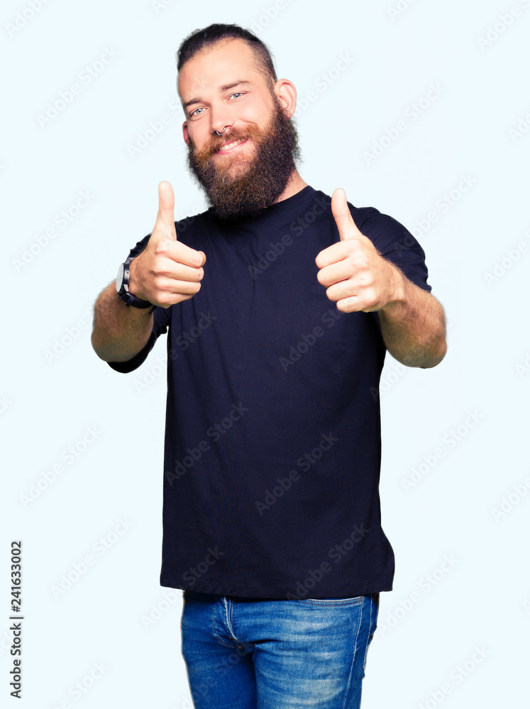 Young blond man wearing casual t-shirt approving doing positive gesture with hand, thumbs up smiling and happy for success. Looking at the camera, winner gesture. Young blond man wearing casual t-shirt approving doing positive gesture with hand, thumbs up smiling and happy for success. Looking at the camera, winner gesture.