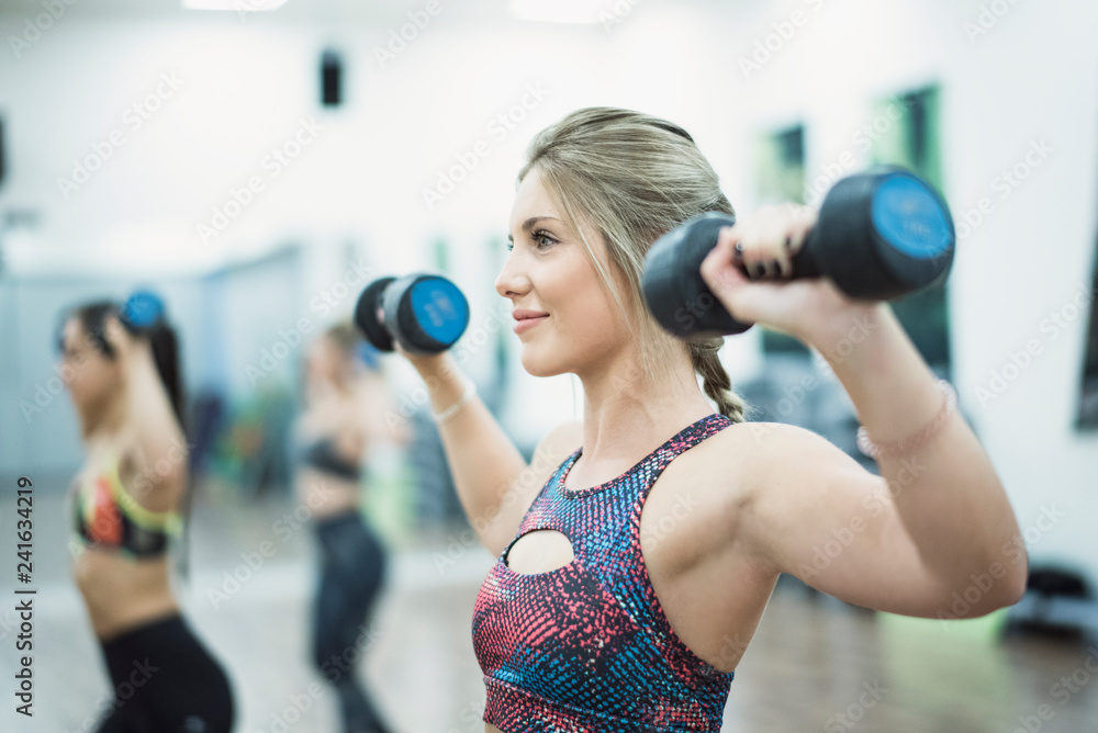 Fototapeta premium Beauty woman training in sport class with dumbbells in gym indoors smiling