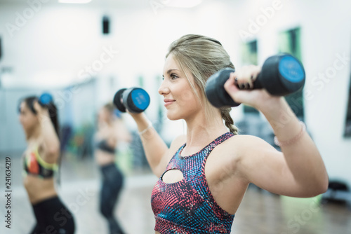 Beauty woman training in sport class with dumbbells in gym indoors smiling
