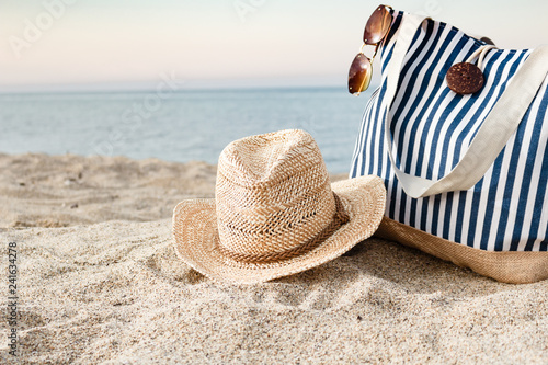 Canvas Print Striped summer bag with straw hat and sunglasses closeup on beach, calm sea background
