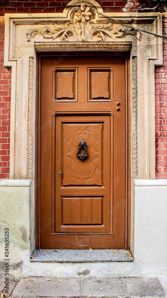 Old Brown Wooden Door with a door knocker floral bas-relief red brick wall Old Brown Wooden Door with a door knocker floral bas-relief red brick wall