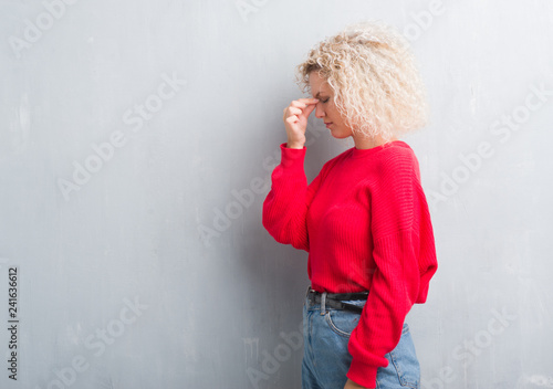 Young blonde woman with curly hair over grunge grey background tired rubbing nose and eyes feeling fatigue and headache. Stress and frustration concept.