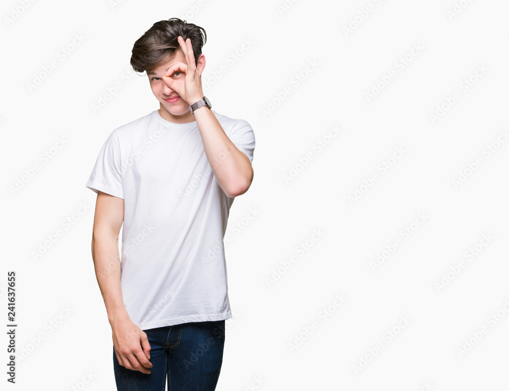 Young handsome man wearing casual white t-shirt over isolated background doing ok gesture with hand smiling, eye looking through fingers with happy face. Young handsome man wearing casual white t-shirt over isolated background doing ok gesture with hand smiling, eye looking through fingers with happy face.