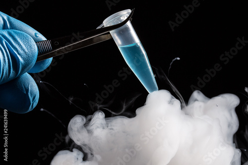 A scientist or lab personal freezes a tube filled with a light blue liquid in it photo