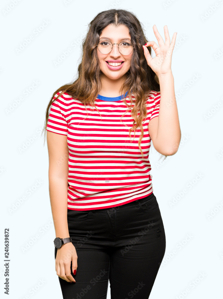 Young beautiful woman wearing glasses smiling positive doing ok sign with hand and fingers. Successful expression.