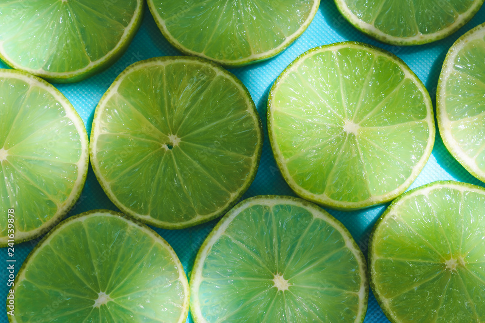 Top view of  green fresh slices of lime on turquoise or blue background in natural lights with shadows. Summer refreshment 