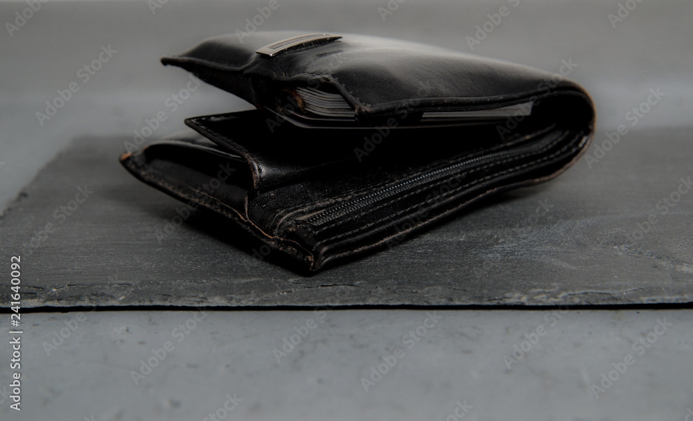 Black leather wallet on a dark, stone counter. The concept of finance, taking care of your own money. Wearing debit and credit cards in the portfolio, care for finances. Black leather wallet on a dark, stone counter. The concept of finance, taking care of your own money. Wearing debit and credit cards in the portfolio, care for finances.