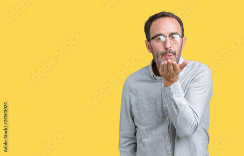 Handsome middle age elegant senior man wearing glasses over isolated background looking at the camera blowing a kiss with hand on air being lovely and sexy. Love expression.