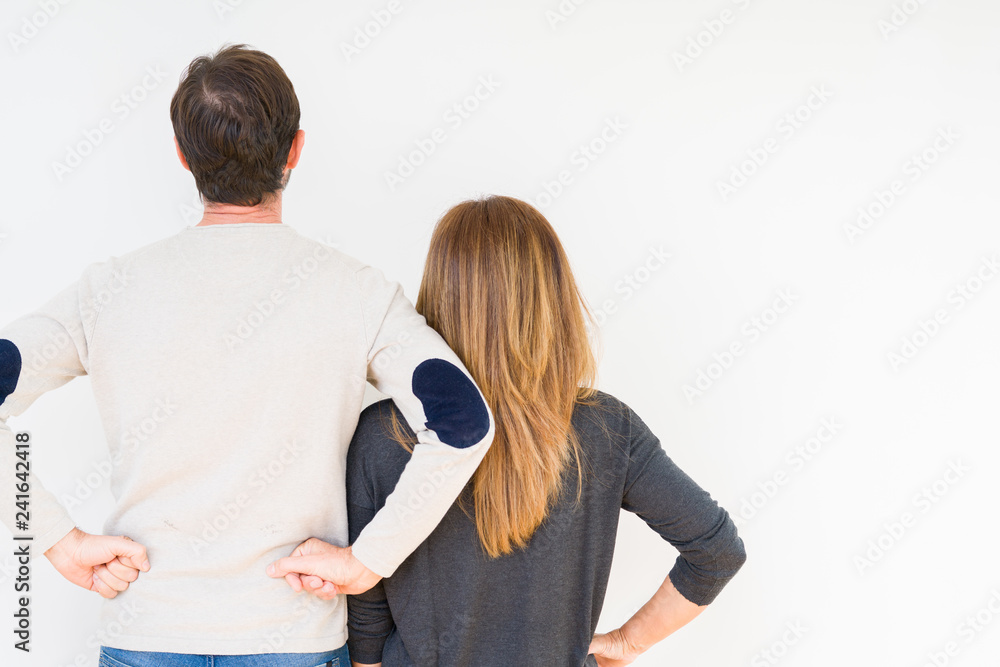 Beautiful middle age couple in love over isolated background standing backwards looking away with arms on body Beautiful middle age couple in love over isolated background standing backwards looking away with arms on body