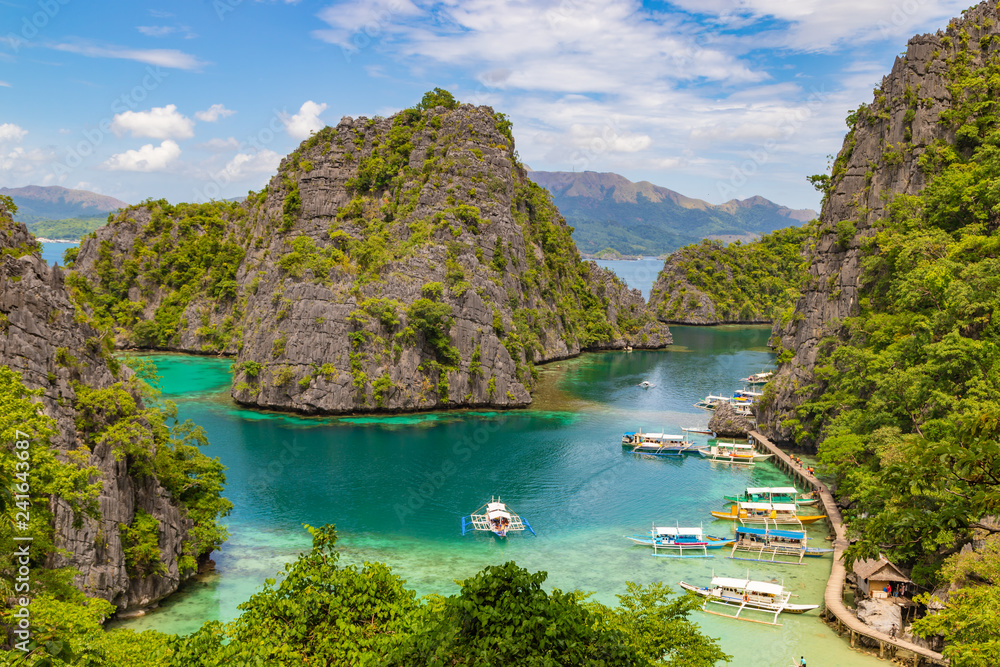 Elevated view of lagoon with boats surrounded by rocks and turquoise sea. Coron. Palawan, Philippines.