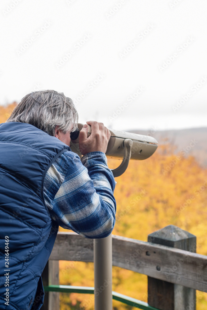 Man looking through binoculars at scenic overlook (vertical)