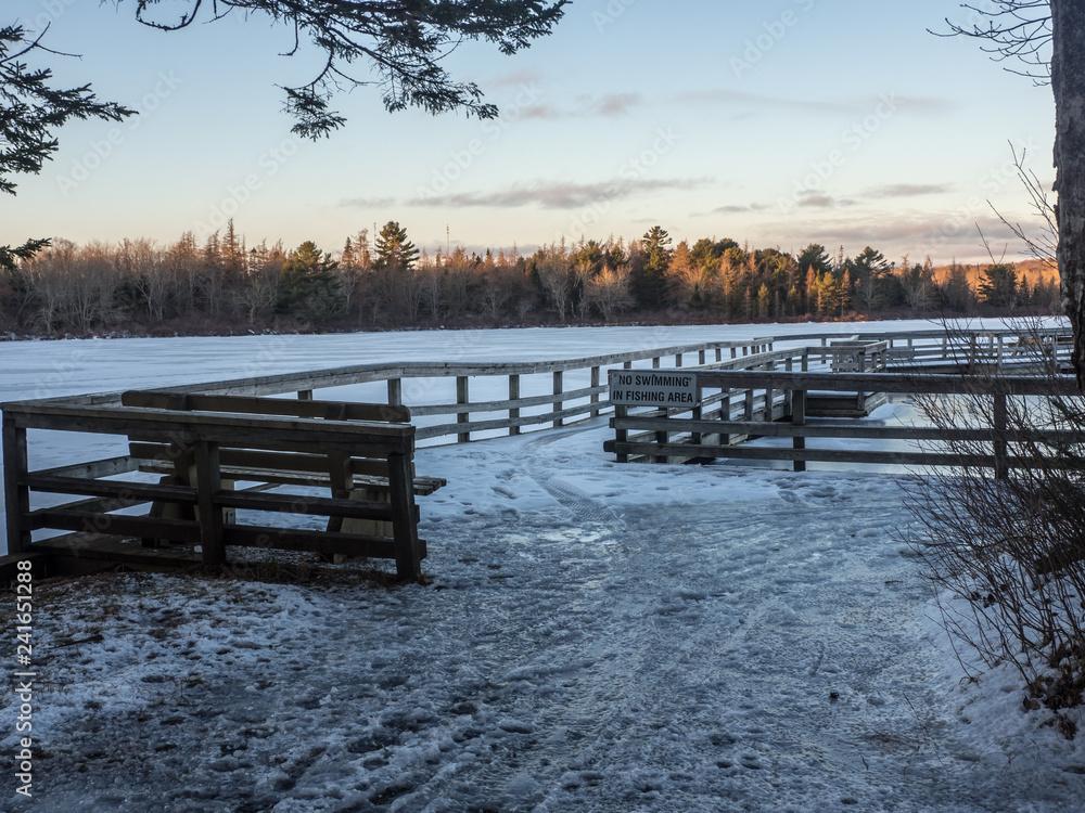 wooden boardwalk in winter covered in ice and snow at sunset