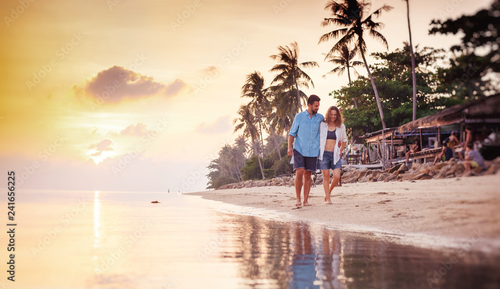 Beautiful young love happy couple walking arm in arm on the beach at sunset during the honeymoon vacation travel