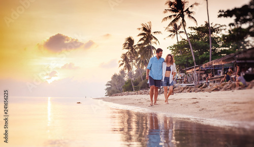 Beautiful young love happy couple walking arm in arm on the beach at sunset during the honeymoon vacation travel photo