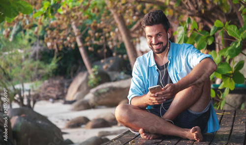 Young attractive man of mixed race guy Latino with a beard listening to music on headphones, outdoors
