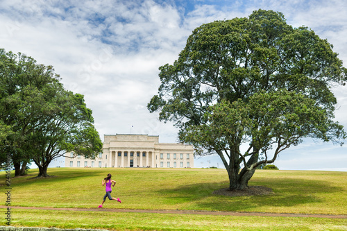 Auckland city park running jogging girl on green grass and trees at Auckland Domain park with Memorial museum . Active lifestyle woman training. Famous travel tourist attraction in New Zealand.