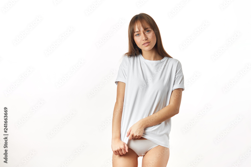 Young attractive woman with soft and smooth healthy skin after laser depilation of her private parts. Slim woman seductively raising up her white t-shirt, isolated on white background. Young attractive woman with soft and smooth healthy skin after laser depilation of her private parts. Slim woman seductively raising up her white t-shirt, isolated on white background.