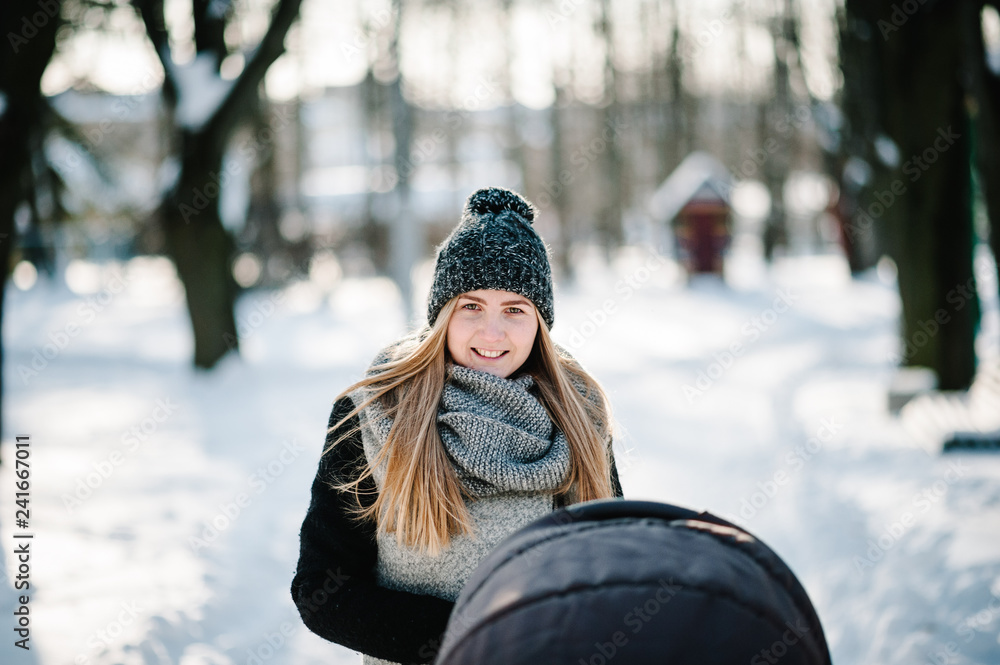 A happy young mother walks with a stroller and baby in a winter park. A happy young mother walks with a stroller and baby in a winter park.