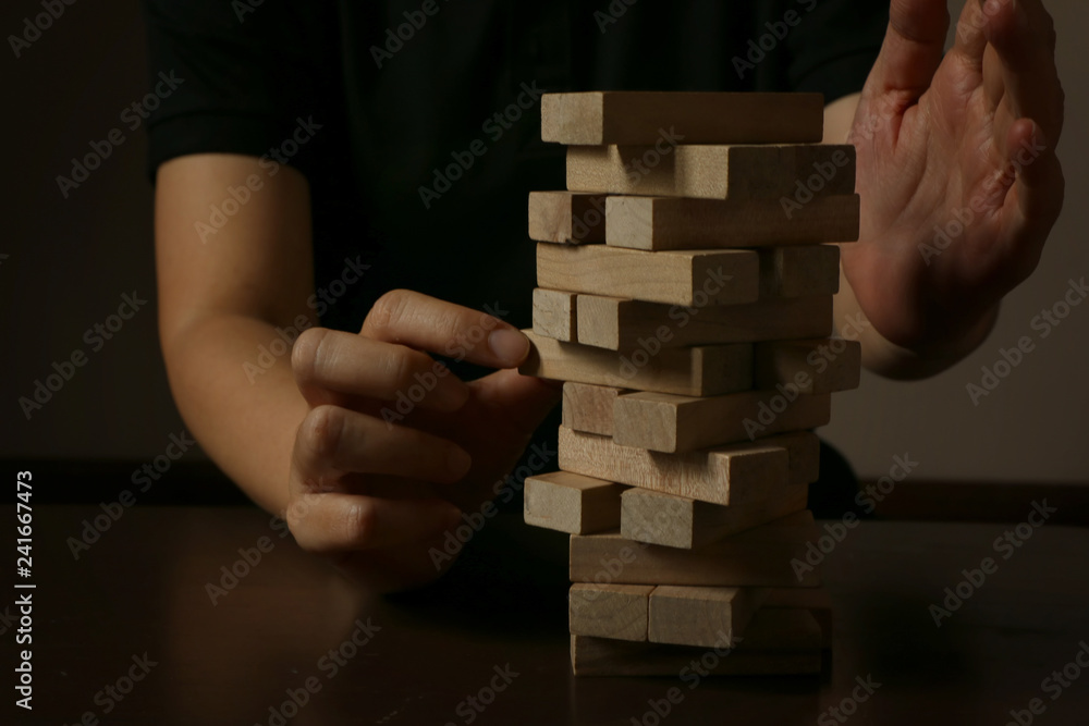 Hand of woman planning, risk and strategy in business.Businessman gambling placing wooden block on a tower and protect it Hand of woman planning, risk and strategy in business.Businessman gambling placing wooden block on a tower and protect it