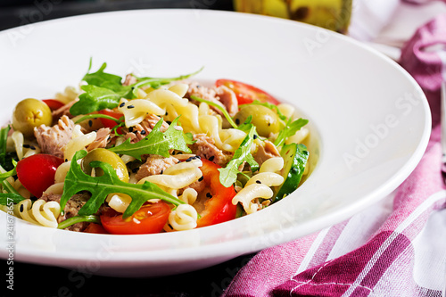 Pasta salad with tuna, tomatoes, olives, cucumber, sweet pepper and arugula on rustic background .