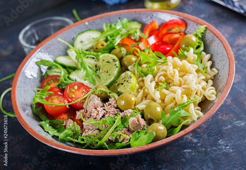 Buddha bowl. Pasta salad with tuna, tomatoes, olives, cucumber, sweet pepper and arugula on rustic background .