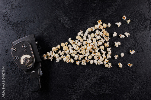 Retro movie camera with popcorn flying out of it on a dark background.