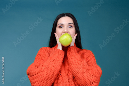 Beautiful surprised young attractive european woman holdin fresh green apple in her teeth. Healthy lifestyle concept. Raw vegetarian organic food.