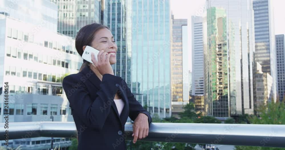 Beautiful young businesswoman talking on mobile phone by railing. Smiling business professional using smartphone while standing against buildings. She is wearing suit in city. Beautiful young businesswoman talking on mobile phone by railing. Smiling business professional using smartphone while standing against buildings. She is wearing suit in city.