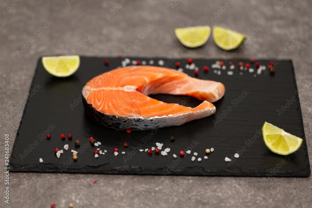 Salmon steak raw fish prepared for cooking with lime and spices. Top view on black slate board. Salmon steak raw fish prepared for cooking with lime and spices. Top view on black slate board.
