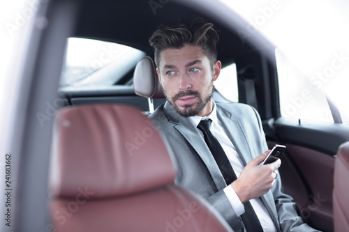 man in suit sitting in car and reading messages on smartphone