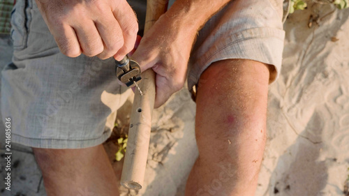 Senior man sits on the beach and making flute by hands, close-up. © alexeg84