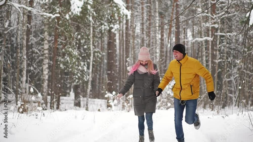 A young and beautiful couple is having fun in the park, running and holding hands. Valentine's Day and love story concept. Winter season. A young and beautiful couple is having fun in the park, running and holding hands. Valentine's Day and love story concept. Winter season.