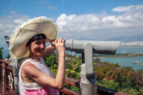 The girl in the hat looks through binoculars on the city bay