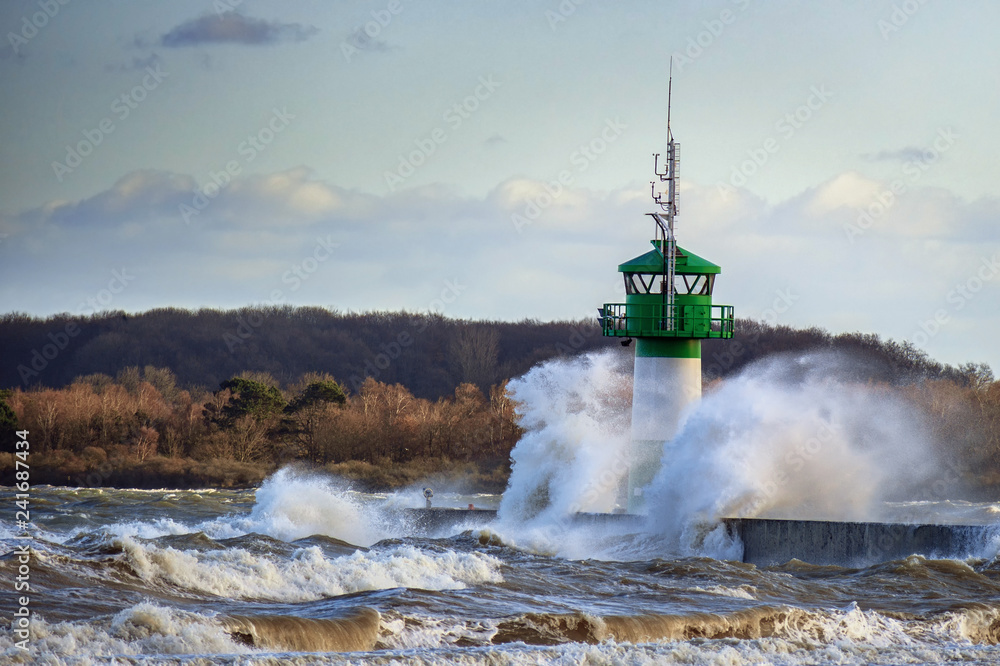 Fototapeta premium lighthouse during storm in splashing spray in Travemuende, tourist destination on the Baltic Sea in the Luebeck bay, copy space