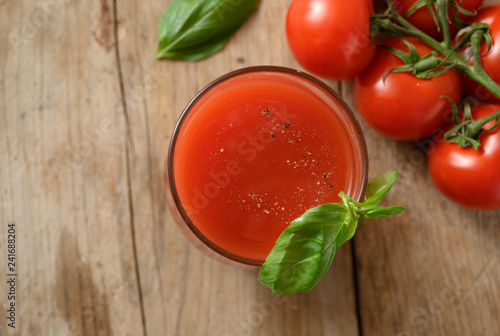 fresh tomato juice in a drinking glass with basil garnish on a rustic wooden board, healthy smoothie drink with copy space, top view from above